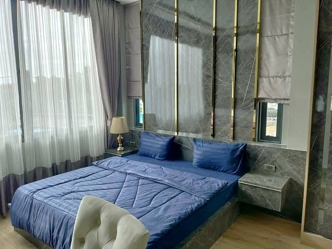 Modern hotel-style bedroom with a blue duvet, two matching blue pillows, and marble wall panels behind the bed.
