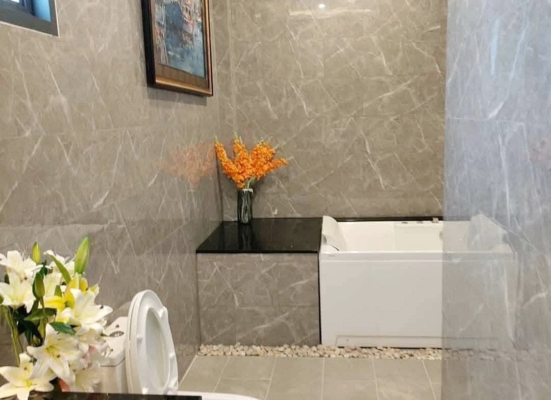 Bathroom with gray marble walls and floor, white bathtub along back wall, black countertop with orange flowers, and a framed painting above.
