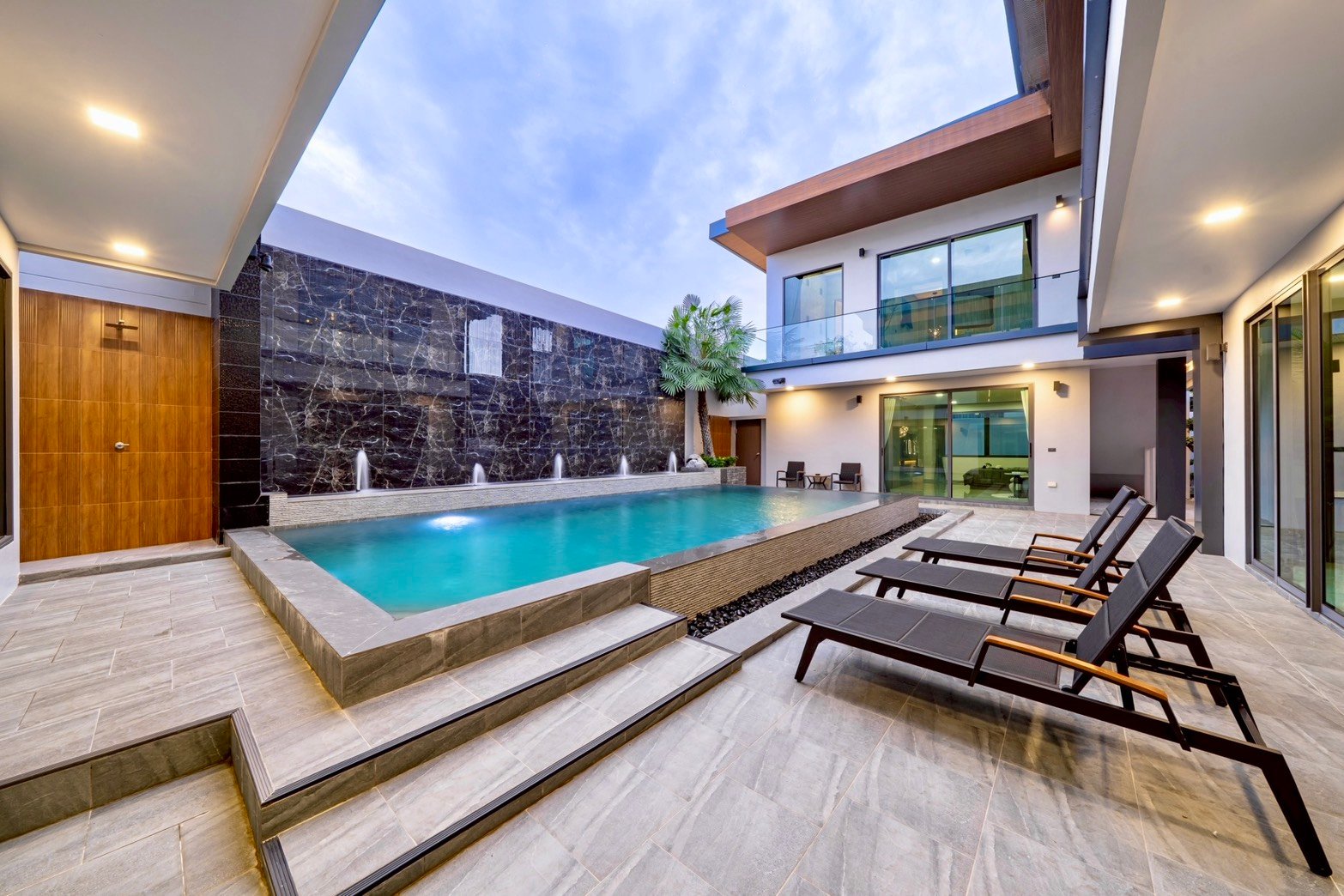 M_Mountain_Dlh518 13 Modern villa courtyard with a rectangular pool, waterfall wall, and lounge chairs on a tiled deck.