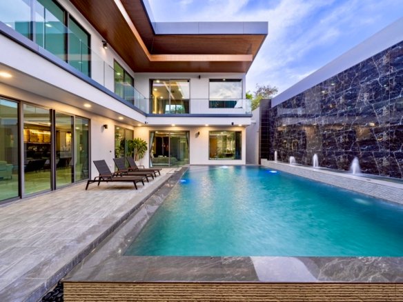 Modern villa backyard with a rectangular turquoise pool, glass railings, and lounge chairs along a tiled deck