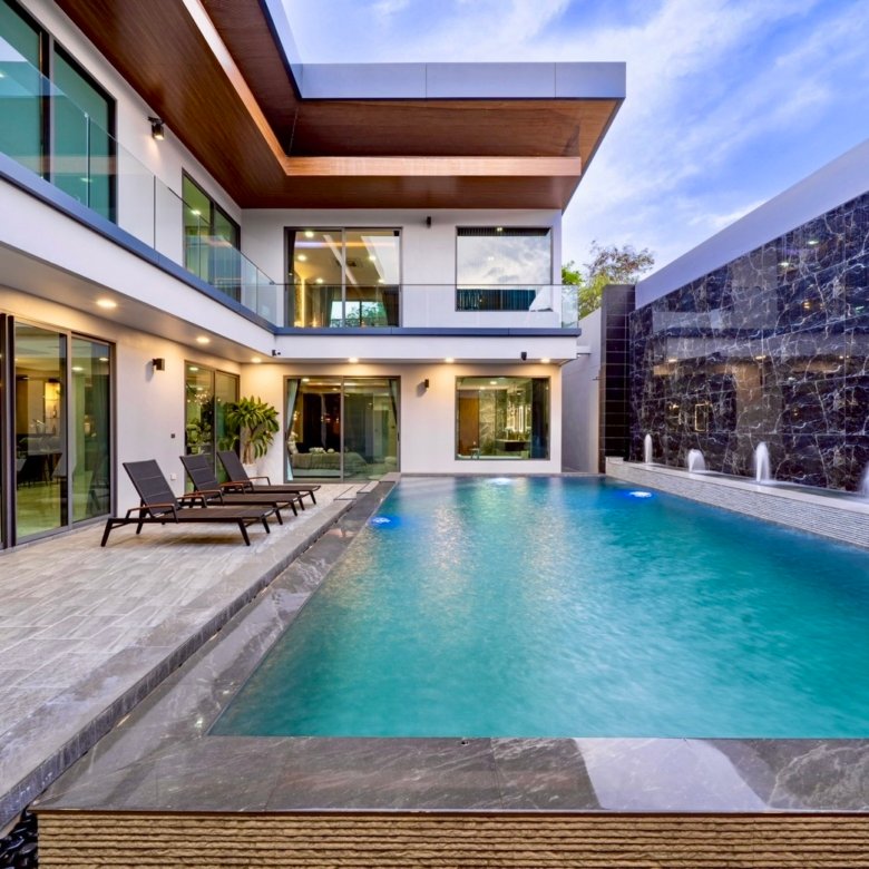 Modern villa backyard with a rectangular turquoise pool glass railings and lounge chairs along a tiled deck