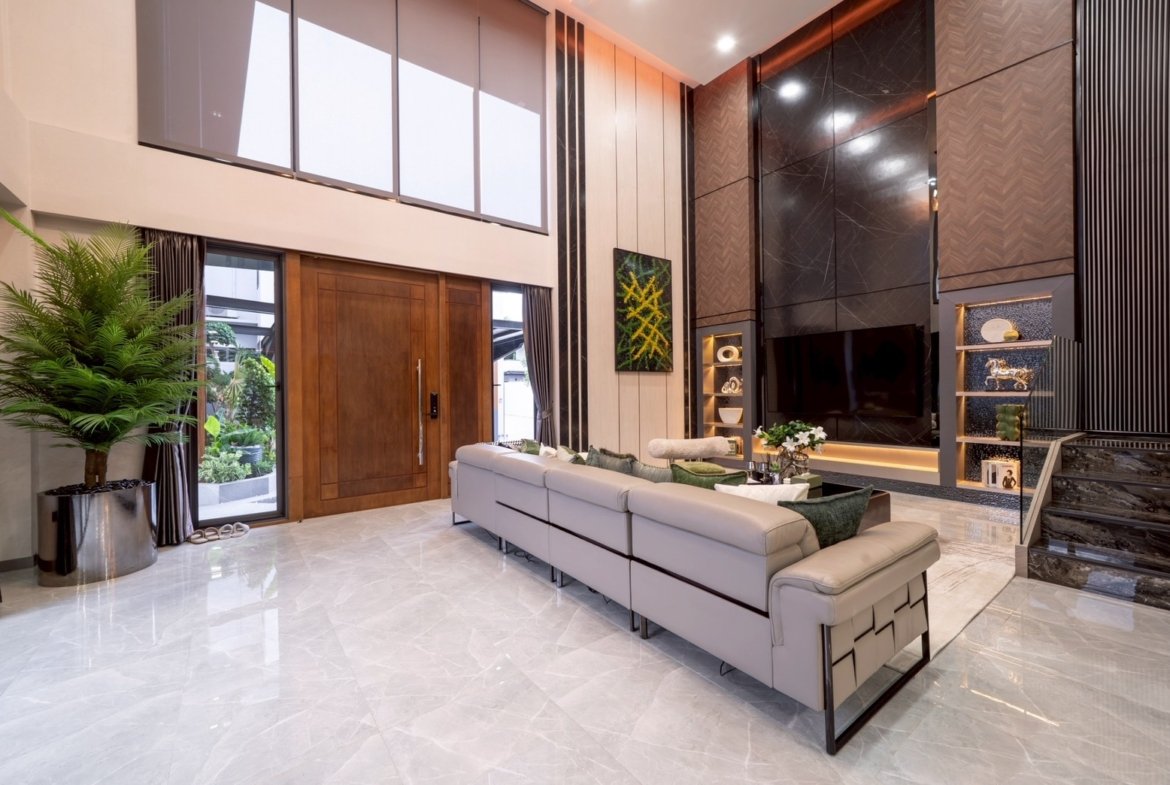 Modern living room with a long light-gray sectional, white marble floor, and a tall wooden front door