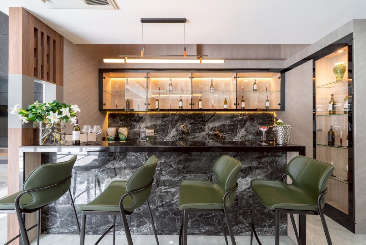 Modern home bar with a black marble counter, glass-front cabinets, and green bar stools.