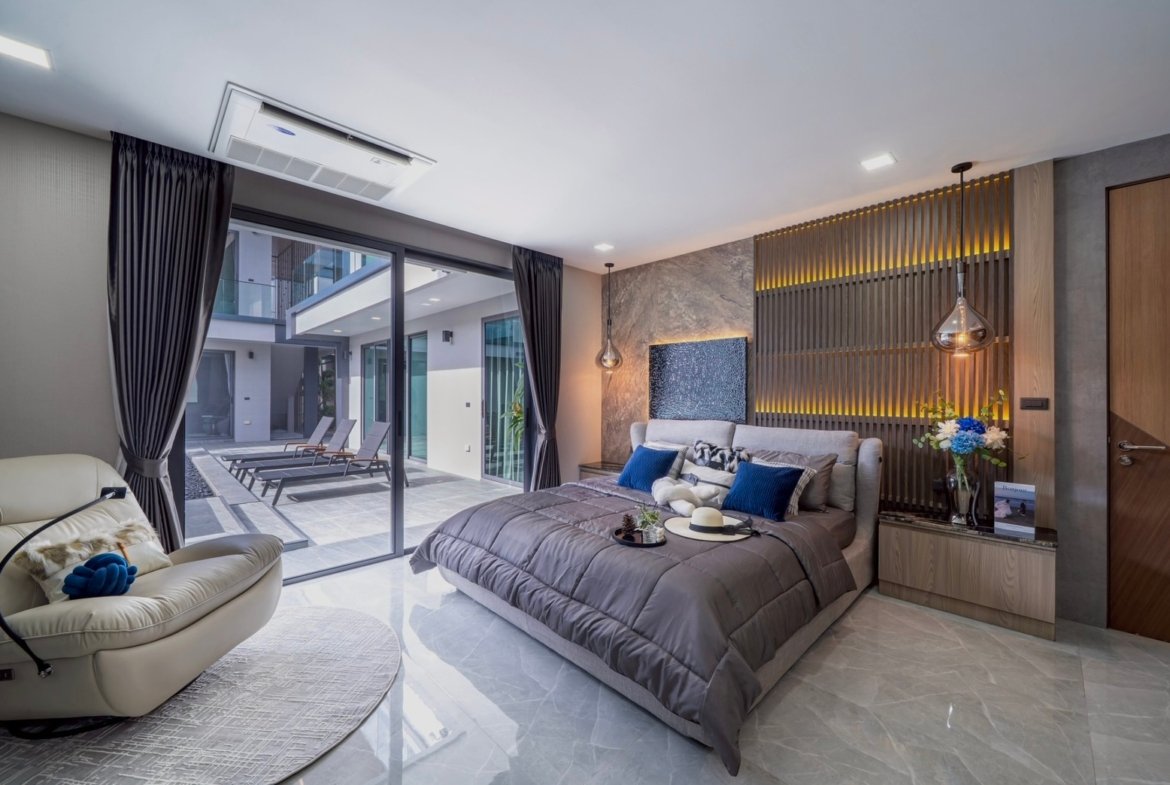 Luxurious bedroom with a large sliding glass door opening to an outdoor pool area and lounge chairs in the courtyard district of a modern home/hotel.