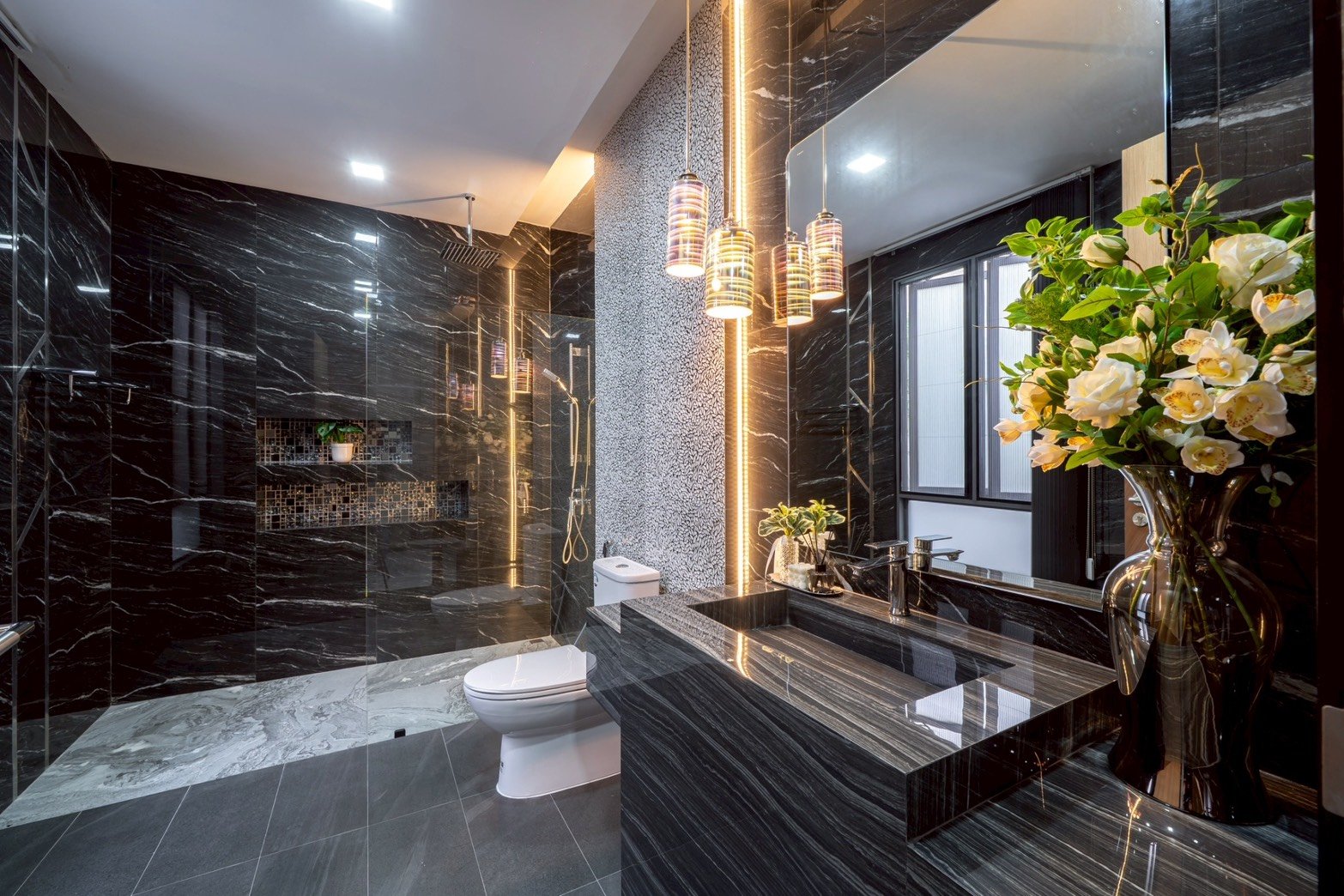 M_Mountain_Dlh518 31 Luxurious black marble bathroom with glass shower, wall-to-wall mirror, and a dark marble vanity topped with a vase of white flowers.