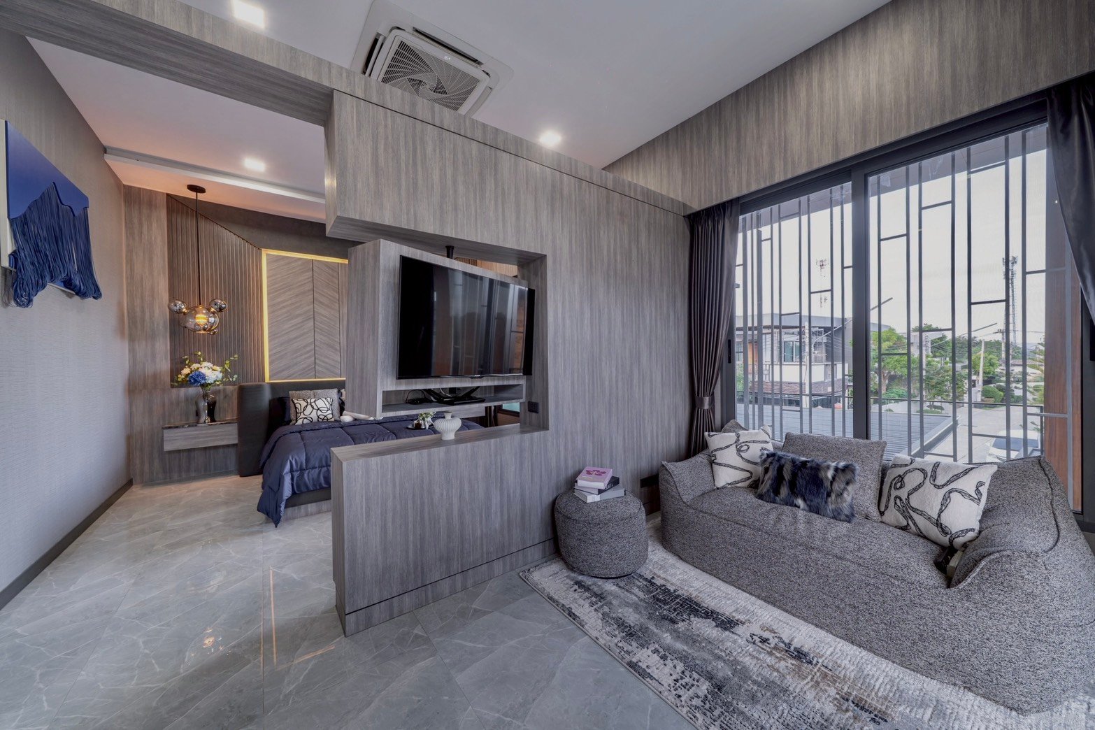 M_Mountain_Dlh518 34 Modern hotel suite with a grey wood-paneled living area, wall-mounted TV, and an open bedroom separated by a partial wall and wardrobe-looking structure, plus large balcony doors.