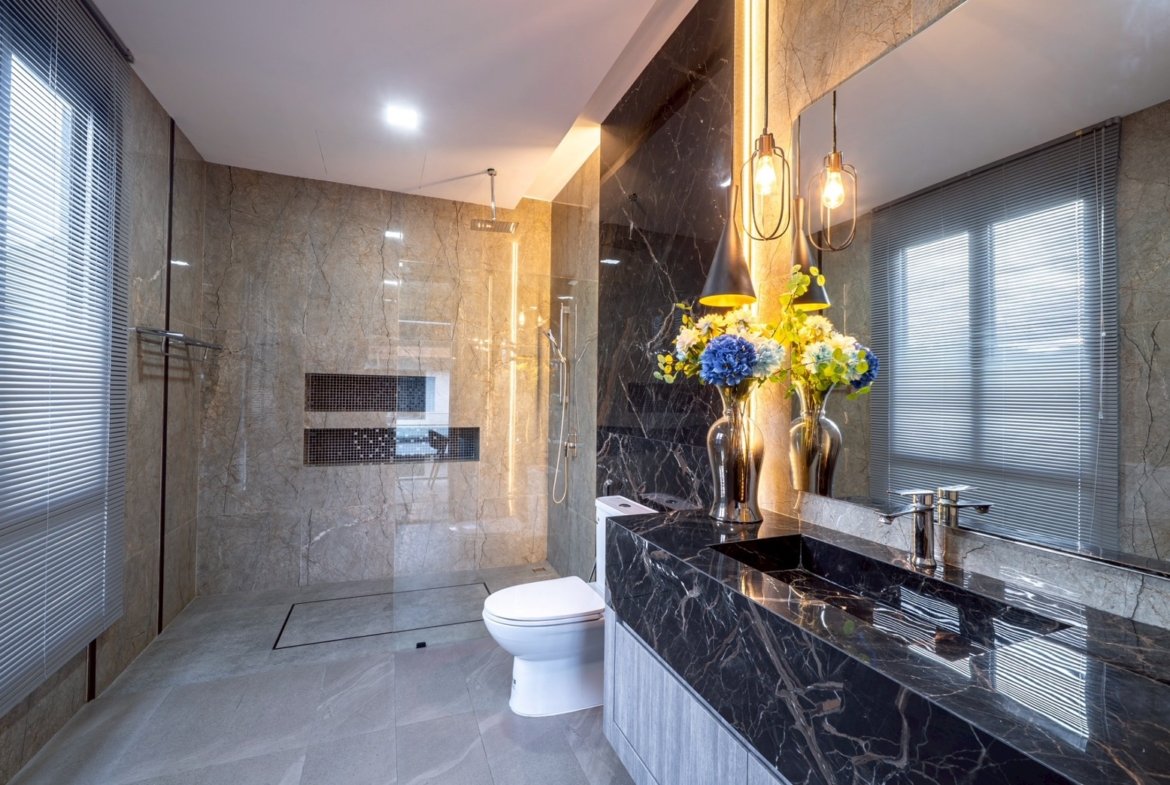 Luxurious bathroom with marble walls and floor, a glass-enclosed walk‑in shower, and a black marble double-sink vanity with a floral arrangement.