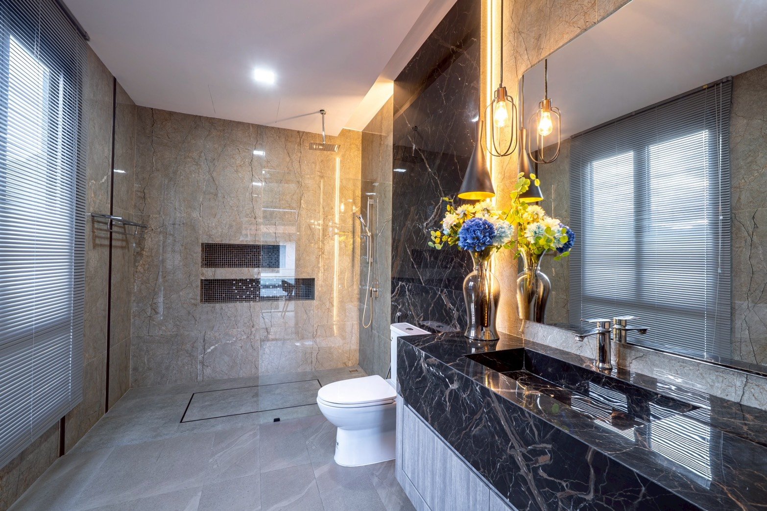 M_Mountain_Dlh518 36 Luxurious bathroom with marble walls and floor, a glass-enclosed walk‑in shower, and a black marble double-sink vanity with a floral arrangement.