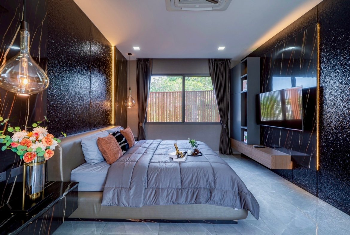 Luxurious modern bedroom with a large gray bed, velvet pillows, and glossy black marble walls with gold veining.