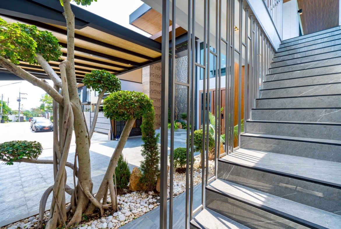 Modern building entrance with gray stone stairs, vertical metal railing, and trimmed trees beside a pebble garden.”,