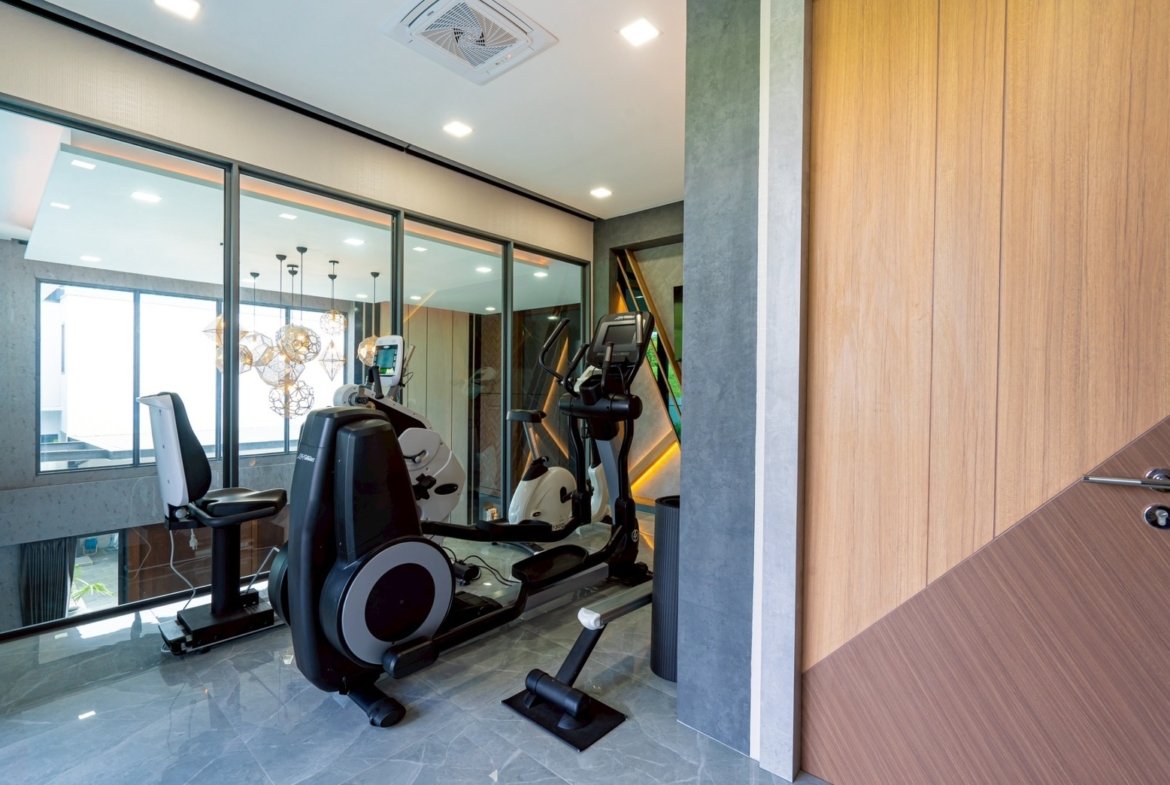 Modern home gym with cardio machines beside a glass partition and sleek gray floors.