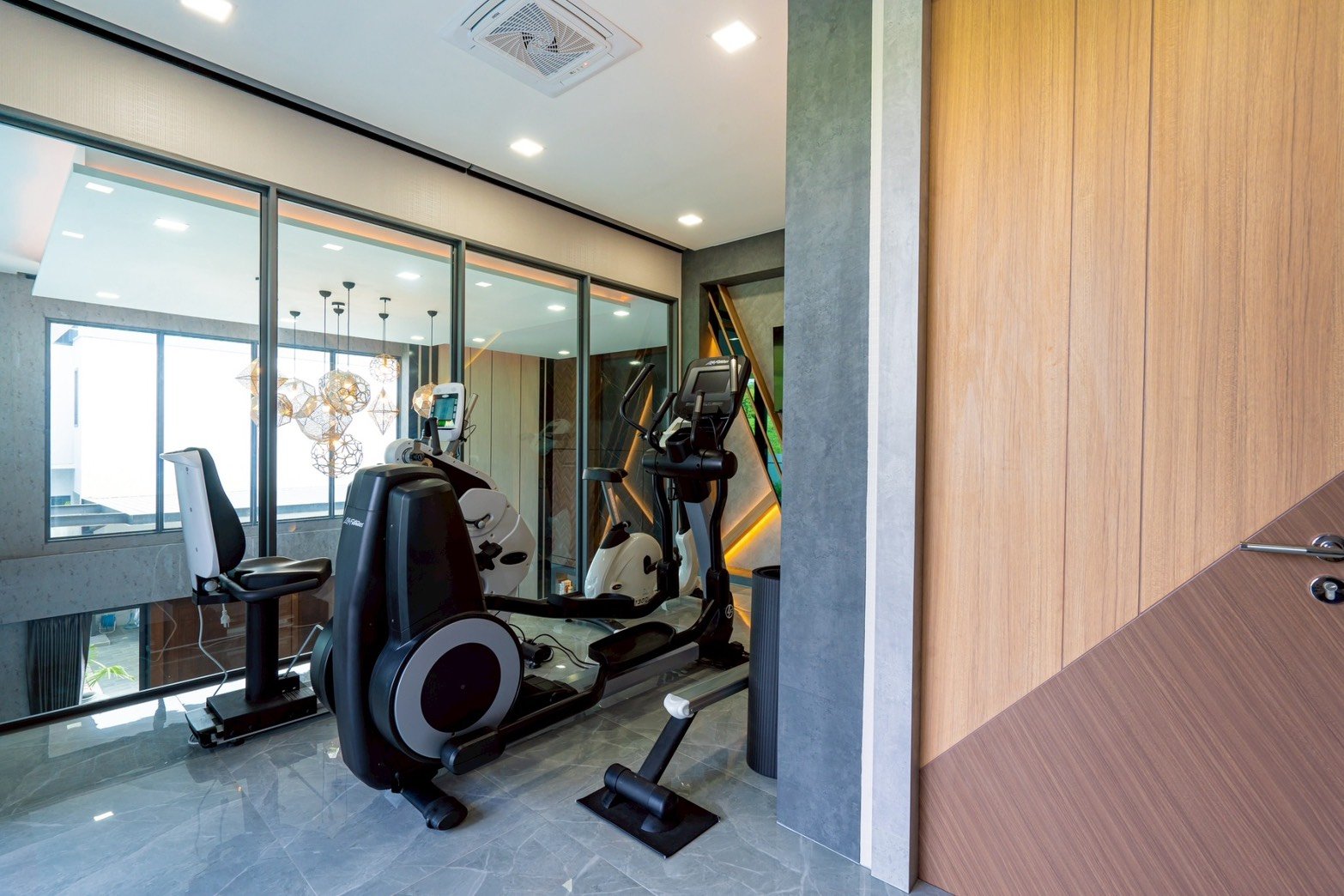 M_Mountain_Dlh518 43 Modern home gym with cardio machines beside a glass partition and sleek gray floors.