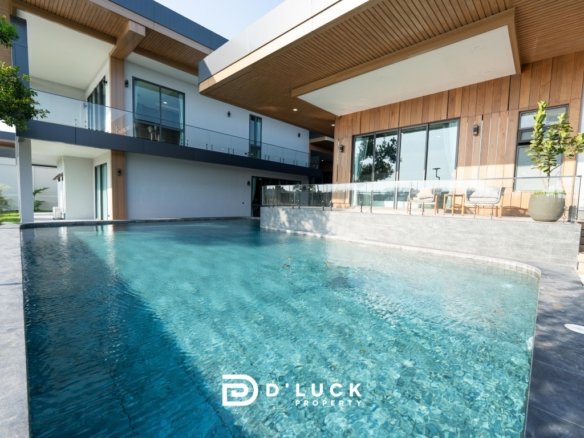 Modern villa with a large rectangular pool in the foreground, featuring wooden accents, glass balconies, and an outdoor seating area on a covered patio.