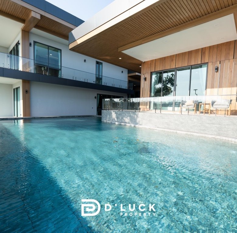 Modern two story home with an expansive turquoise pool glass railings and wooden exterior accents outdoor seating area visible beyond the pool