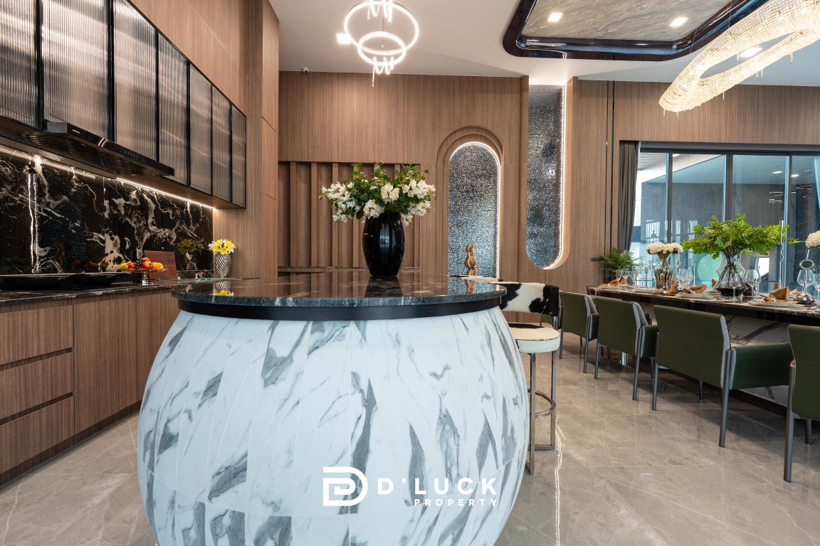 Modern kitchen and dining area with a round marble island, wooden cabinetry, and a long table set for guests.