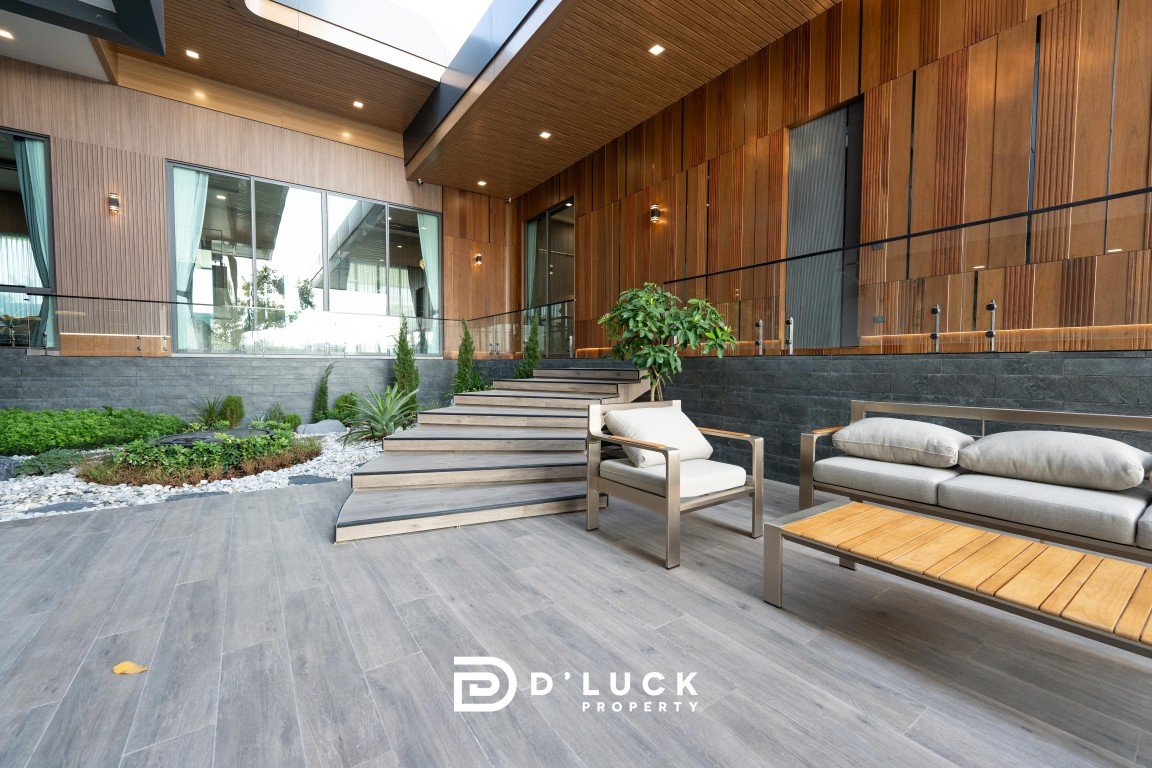Modern outdoor lounge area with gray cushioned seating, wooden accents, and a stepped deck leading to glass doors under a log-style wall lighting paneling.