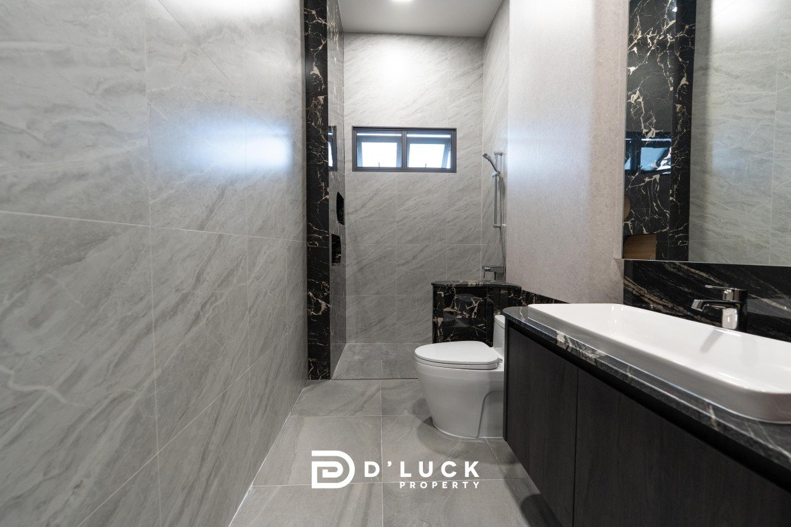 Modern marble bathroom with grey walls and floors, black marble trim, white sink on a dark vanity, toilet, and a shower at the far end beneath a small window; floor shows D'LUCK PROPERTY logo.