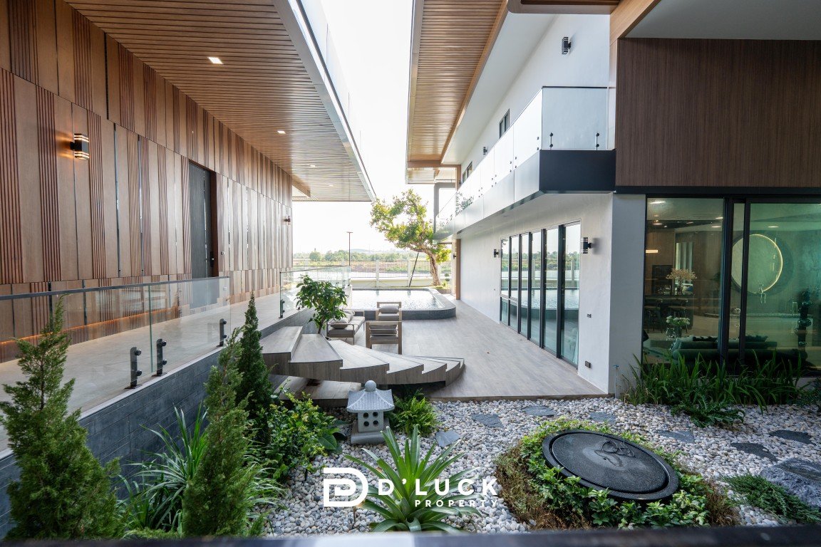 Modern outdoor courtyard between a wood-clad wall and glass-fronted building, with a seating area and greenery, plus the D Luck Property logo at the bottom.