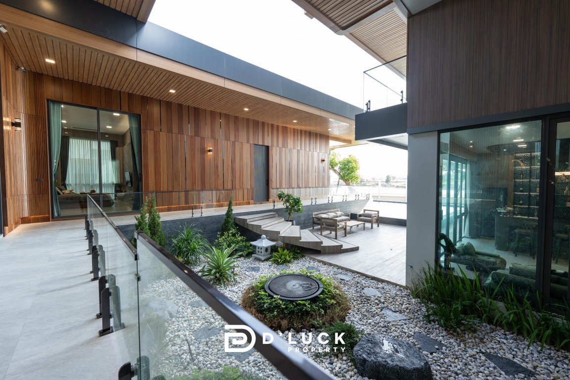 Modern outdoor courtyard of a luxury property with wooden wall panels, glass railing, and a pebble garden with seating area and water feature.