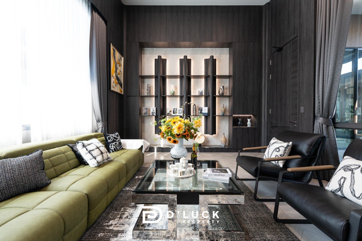 Modern living room with an olive-green sectional, black leather chairs, and a glass coffee table with a sunflower centerpiece.