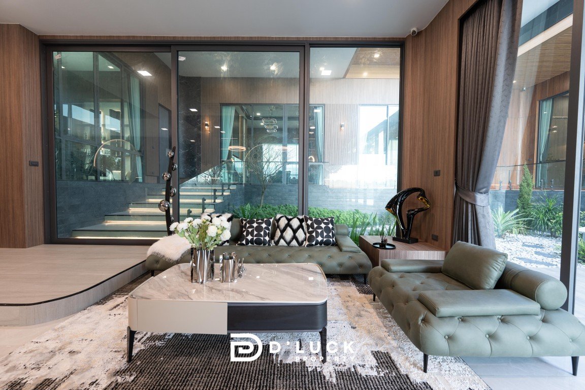 Modern living room with a green tufted sofa, glass doors, and a marble coffee table with vases and pillows on a patterned rug.