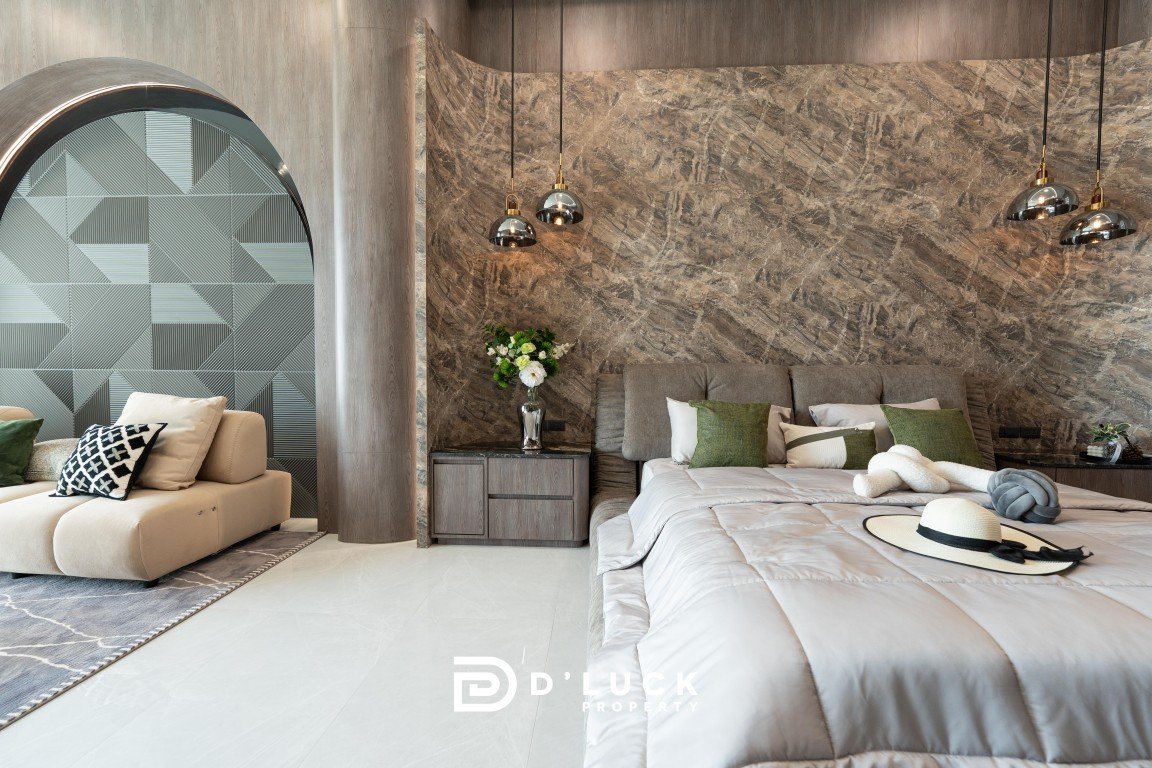 Luxurious hotel bedroom with a large bed, gray bedding, marble textured wall, pendant lights, and a beige seating area with cushions.