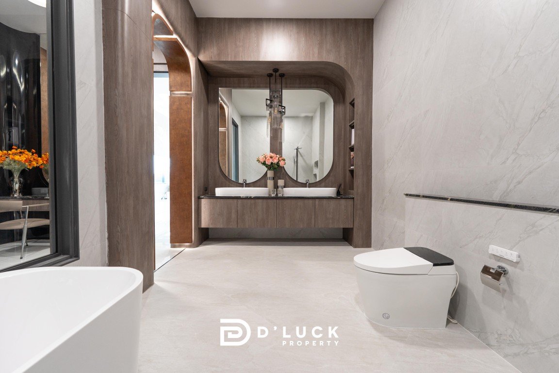 Modern bathroom with a floating wooden vanity, two oval mirrors, and a pink flower centerpiece; white sinks and chandelier visible.