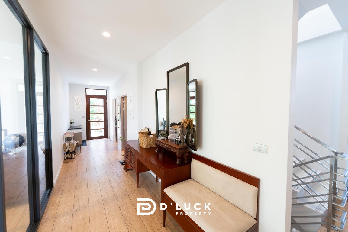 Bright, modern entryway with a long wooden console, three mirrors, baskets and decor along a white wall, beige cushioned bench, and a metal railing staircase to the right.