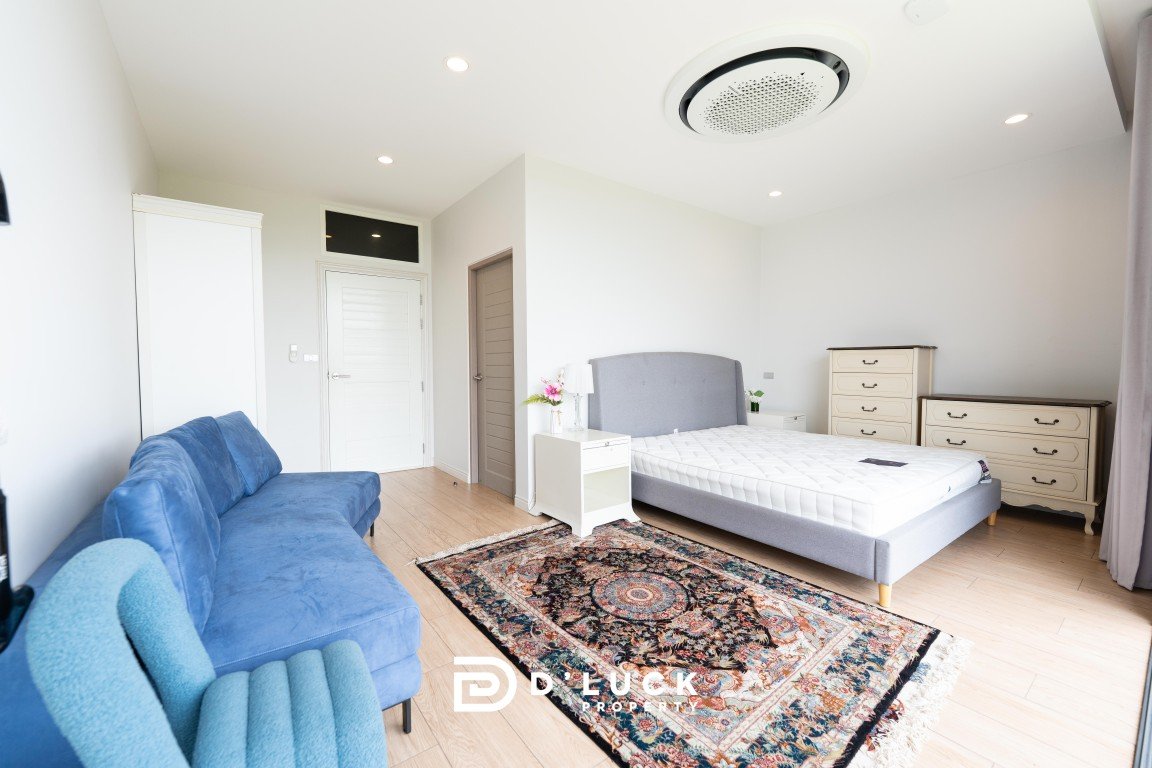 Bright modern bedroom with a gray upholstered bed, white nightstands, cream dressers, a blue sofa, and an ornate rug.