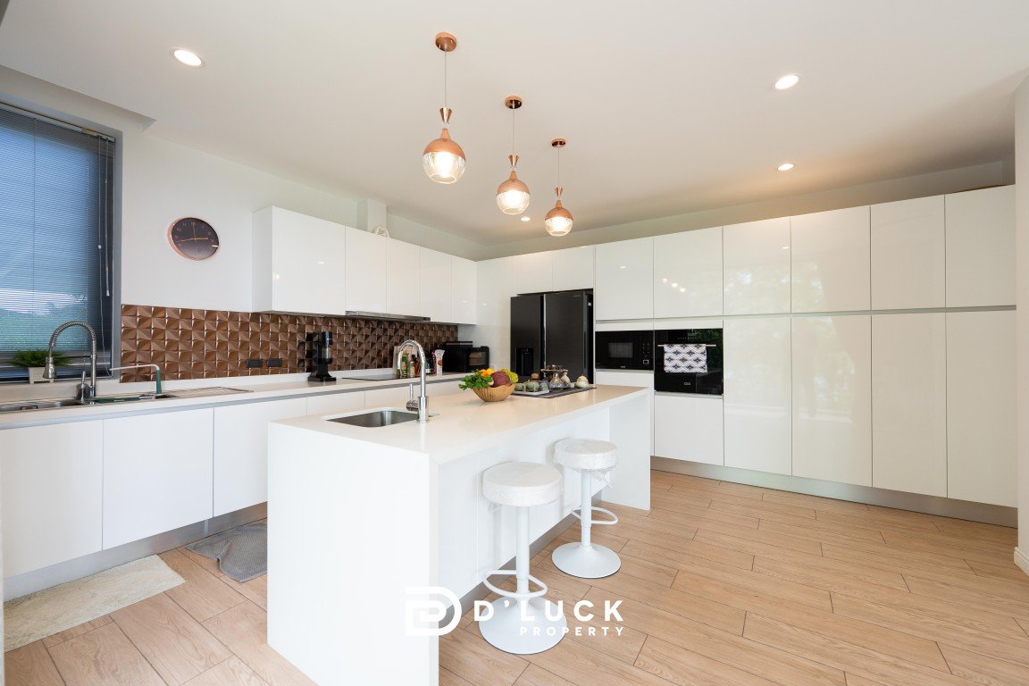 Modern white kitchen with island, copper pendant lights, and built-in appliances (fridge and oven)