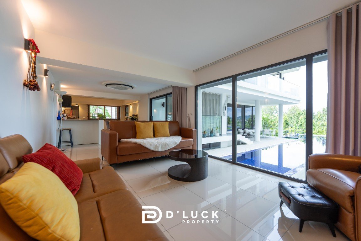 Bright, open living room with tan leather sofas, colorful cushions, and glass doors opening to a poolside terrace.