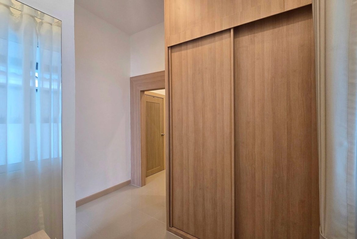 Indoor hallway with a large wooden wardrobe featuring sliding doors on the right, doorway ahead, and sheer white curtains on the left.