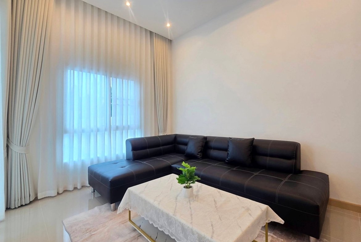 Living room with a black leather sectional, white marble coffee tables with lace cloths, and tall windows with sheer curtains.