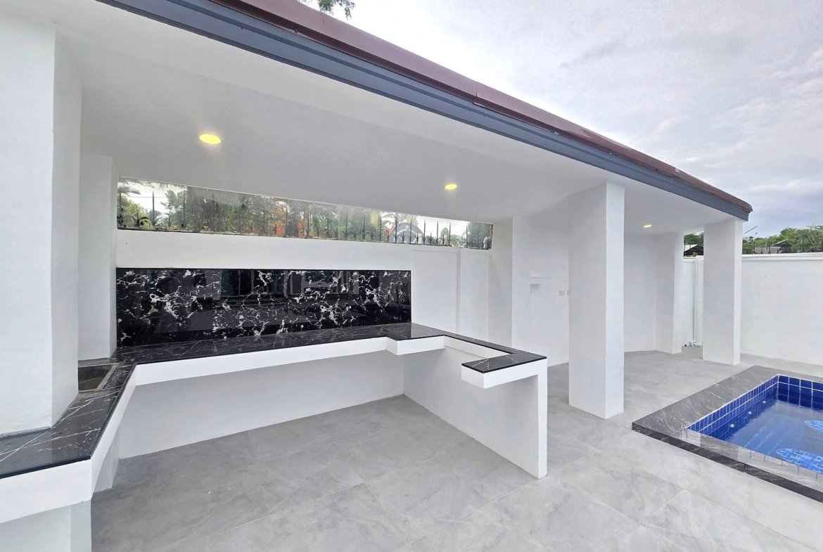 Modern outdoor kitchen with white columns, black marble backsplash, and built-in countertop under a white roof; a blue-tiled pool is visible in the foreground/right.