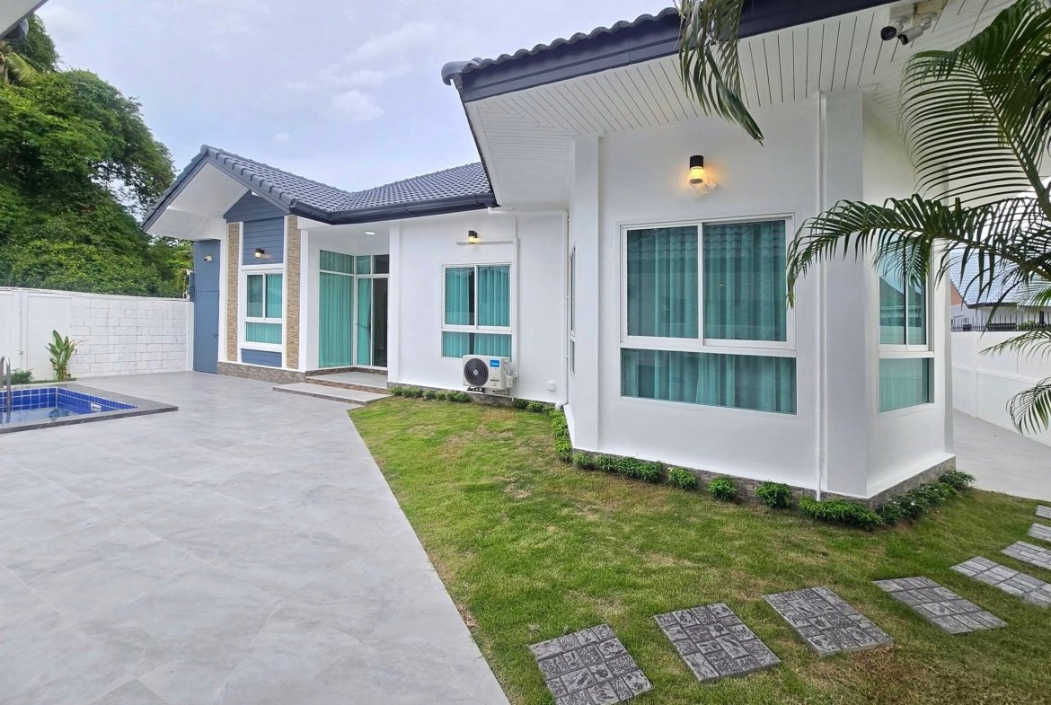 Contemporary white house with large windows, blue-grey accents, and a small pool on a tiled patio area.
