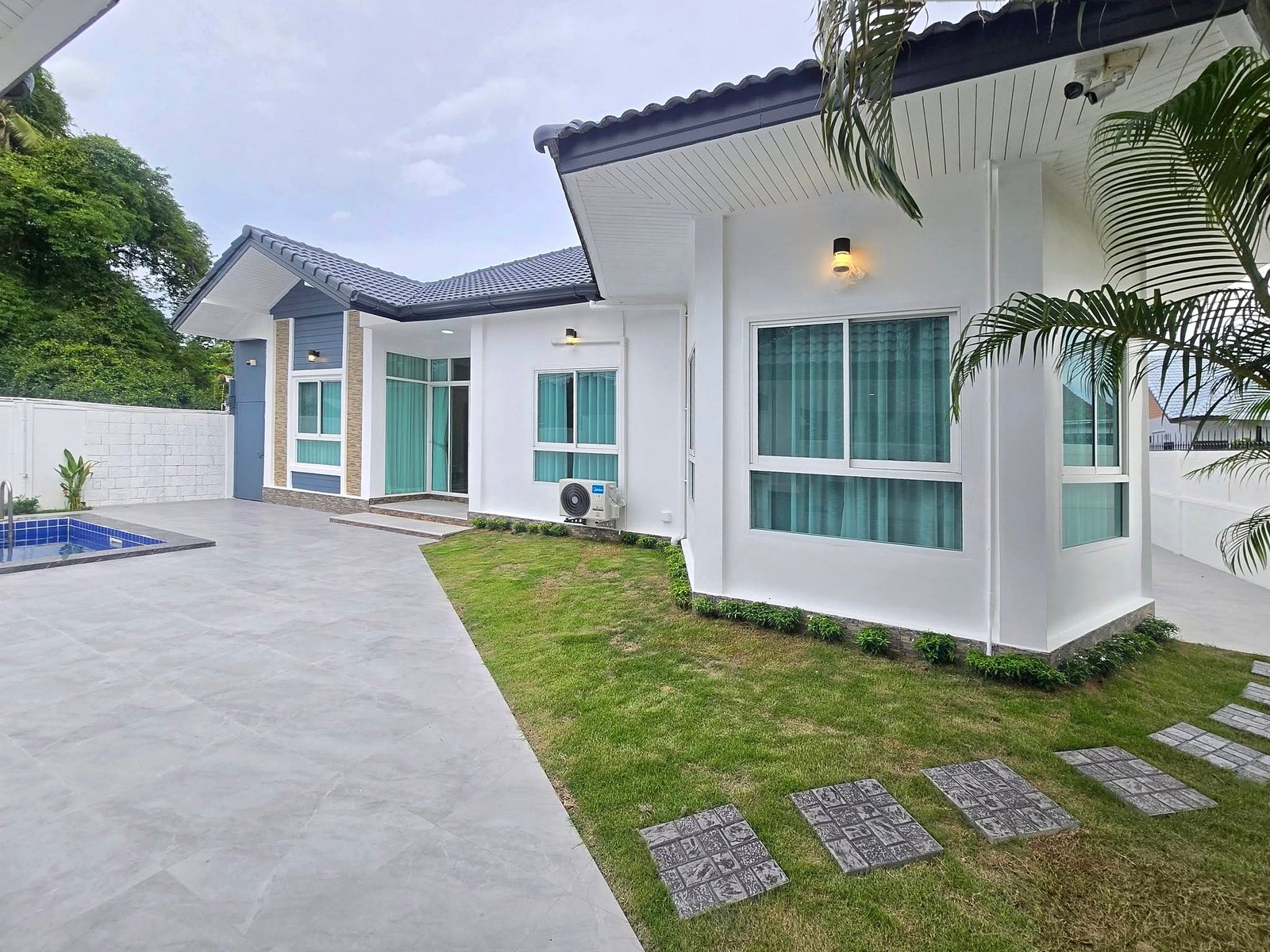Mabprachan_Pool_Villa_Pattaya_Dlh571_2 Contemporary white house with large windows, blue-grey accents, and a small pool on a tiled patio area.