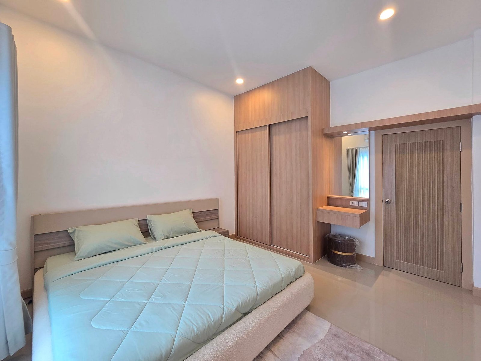 Mabprachan_Pool_Villa_Pattaya_Dlh571_5 Bedroom with a large bed in pale blue bedding, and built-in wooden wardrobe and vanity along the right wall, lit by ceiling lights.