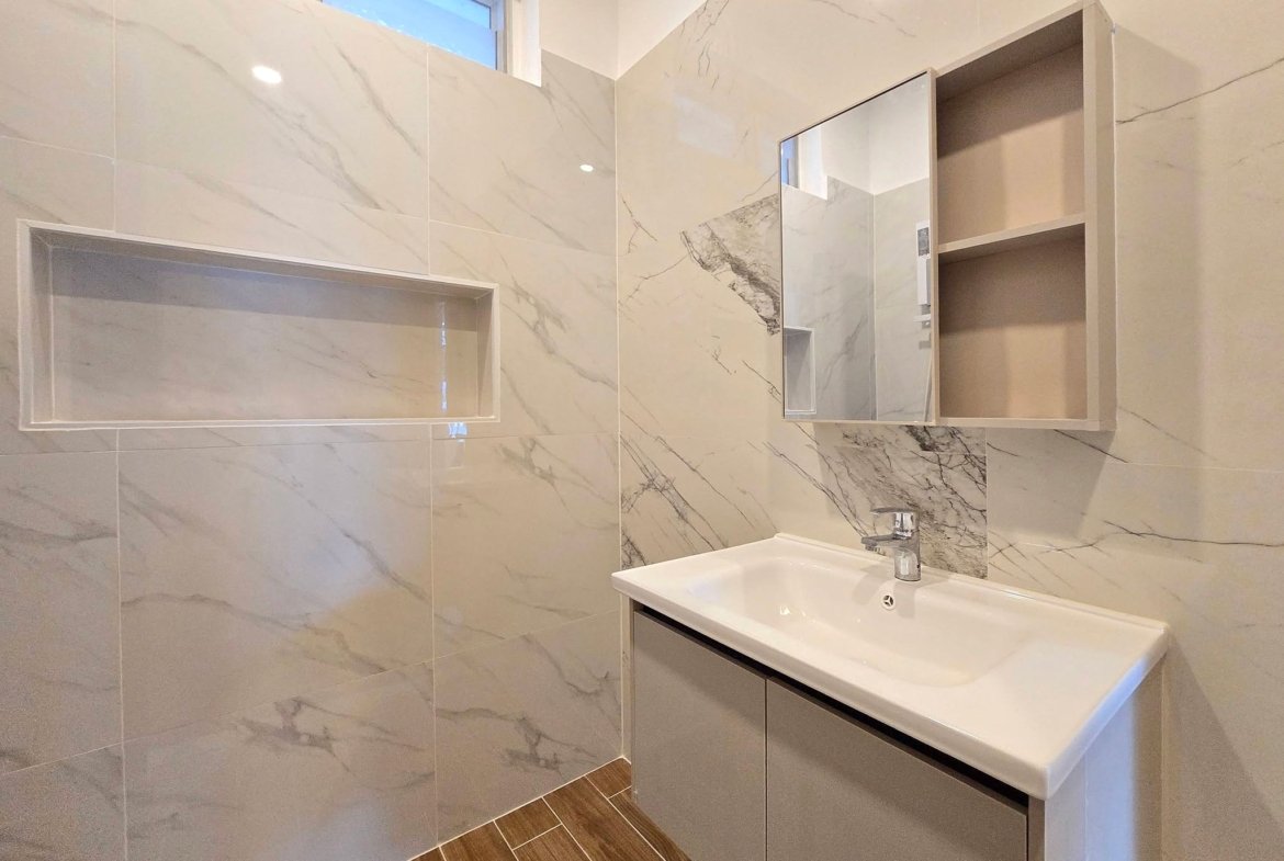 Modern bathroom with gray marble tile walls and a white sink vanity with storage drawers.