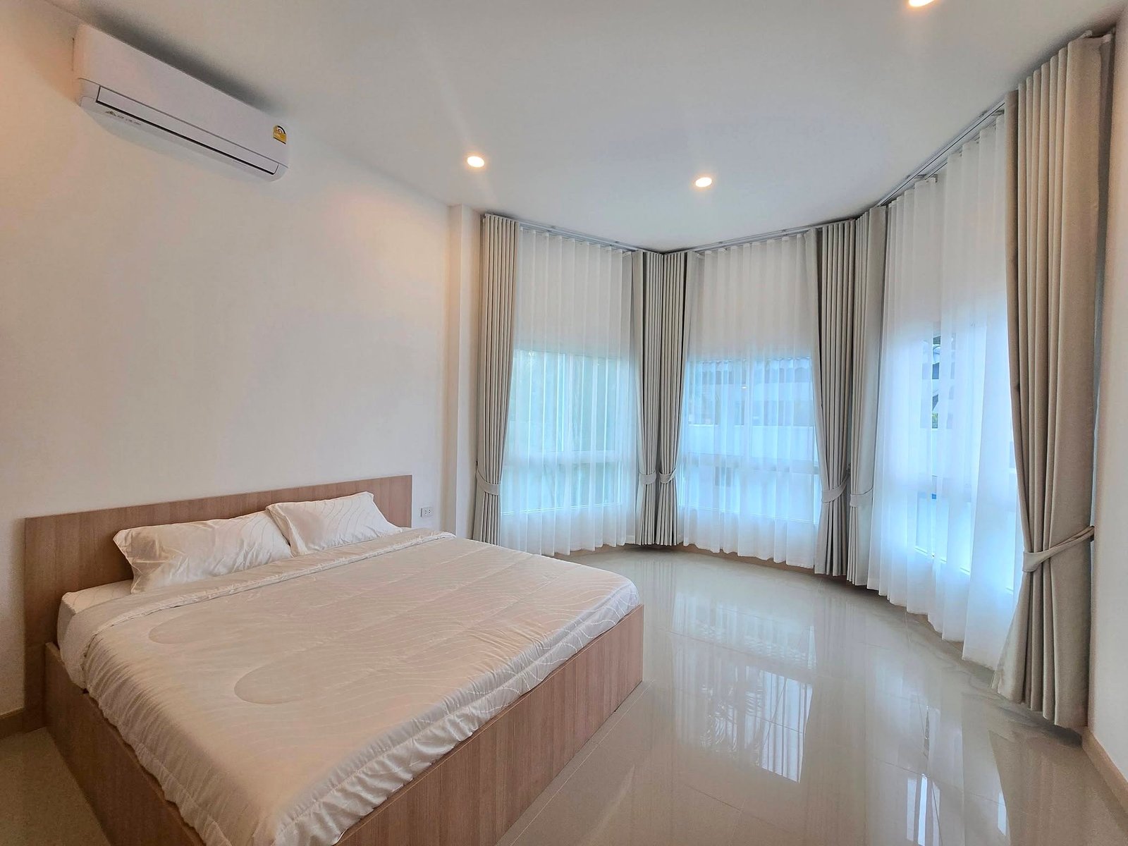 Mabprachan_Pool_Villa_Pattaya_Dlh571_8 Twin-bed hotel room with white linens, wooden headboard, and glossy tiled floor; large windows with sheer and thick curtains along curved wall.
