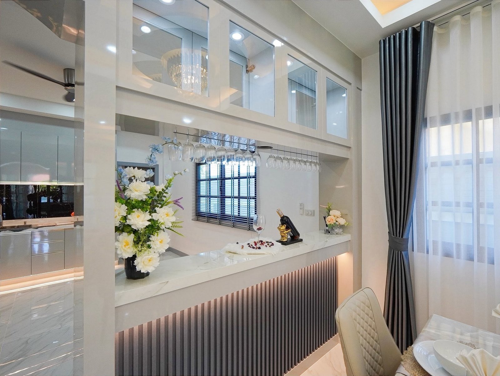 Mabprachan_Village_Pattaya_Dlh564_10 Modern kitchen/bar with wine glass rack, hanging glasses, and marble counter beneath white cabinets. Flowers and decorative items add elegance.