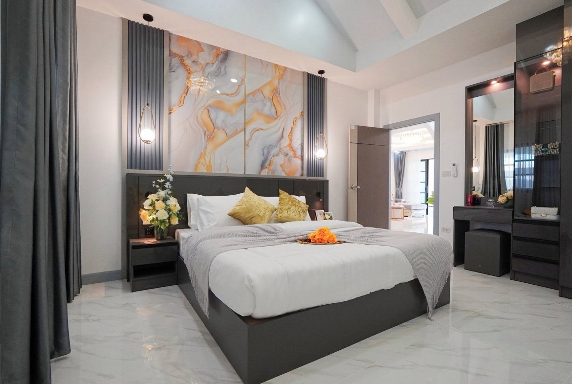 Modern hotel bedroom with a dark wood platform bed, marble accent wall, and gray bedding with yellow cushions.
