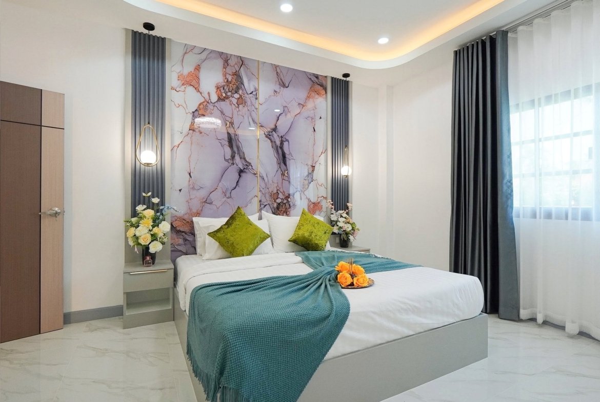 Modern hotel bedroom with a marble-pattern headboard, teal bed throw, green pillows, and fresh flowers on the nightstands.ise