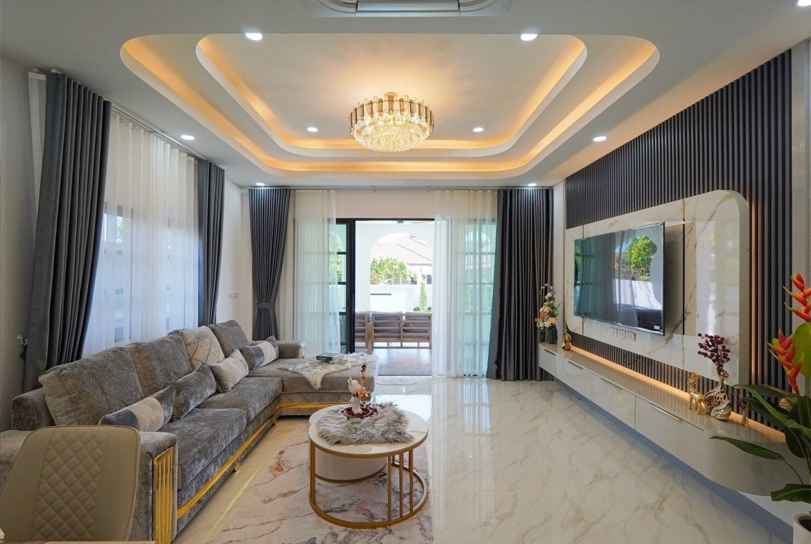 Luxurious living room with a crystal chandelier, layered ceiling arches, and a gray sectional sofa.