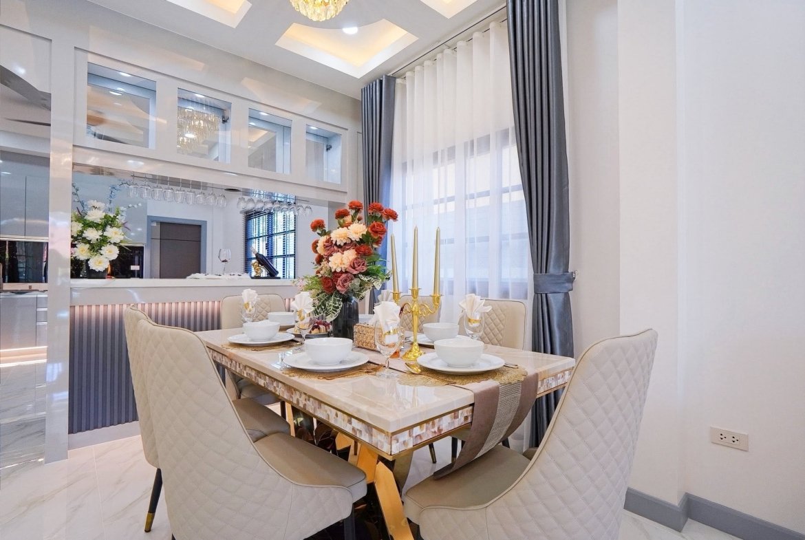 Elegant dining area with a marble table set for six, gold candlesticks, and a floral centerpiece under a chandelier.