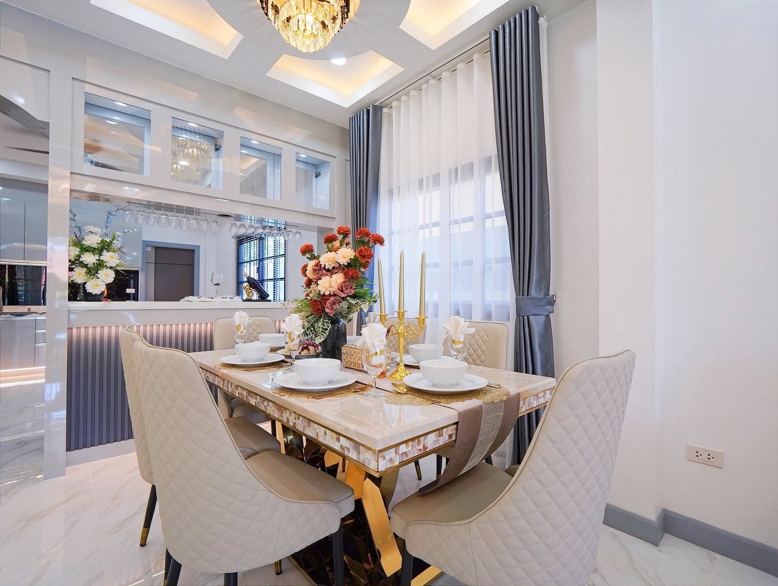 Mabprachan_Village_Pattaya_Dlh564_4 Elegant dining area with a marble table set for six, gold candlesticks, and a floral centerpiece under a chandelier.