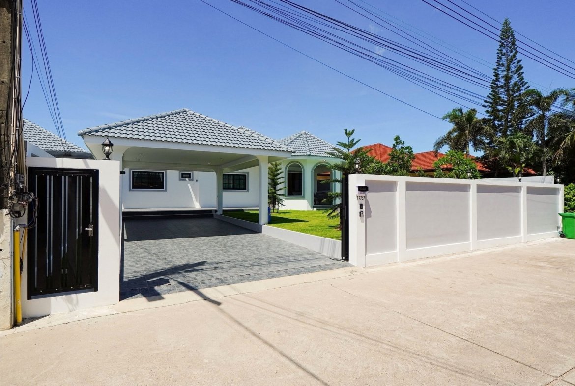 White modern house with a tiled gray roof, driveway, and a gated entrance under a clear blue sky with overhead power lines.
