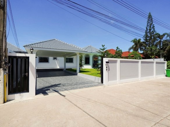 White modern house with a tiled gray roof, driveway, and a gated entrance under a clear blue sky with overhead power lines.