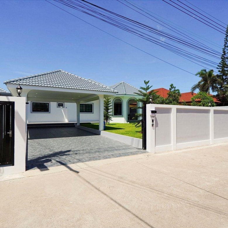 White modern house with a tiled gray roof driveway and a gated entrance under a clear blue sky with overhead power lines