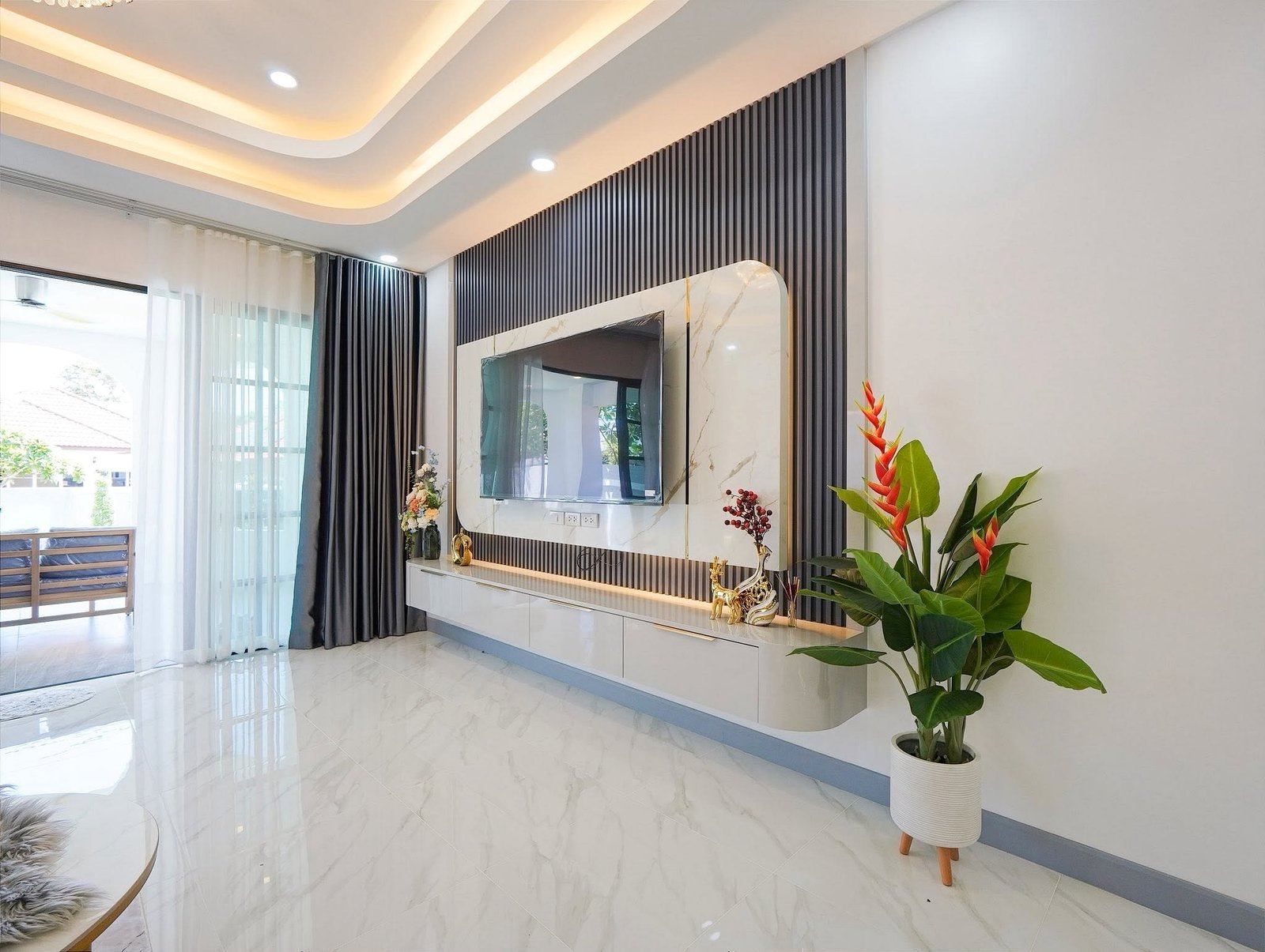 Modern living room with a wall of vertical black panels, a mounted TV, and a marble-framed console area with decor.]