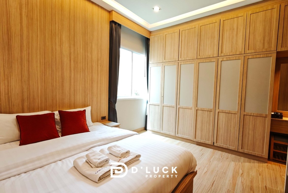 Hotel bedroom with two white beds and red pillows, wooden wall panels, and a large built-in wardrobe along the right wall.
